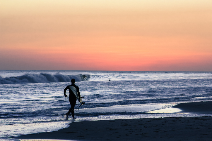 Young man walking on the beach during sunsetSurfer running towards waves during the sunset